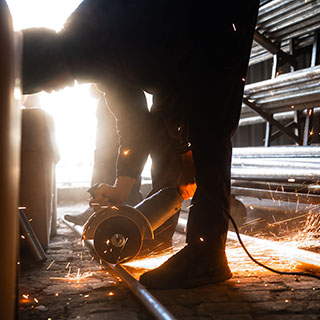 Majstor seče metalnu cev ugaonom brusilicom u radionici.